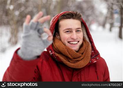 people, christmas, winter and season concept - happy smiling man in hood and scarf outdoors showing ok hand sign