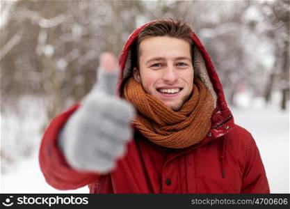 people, christmas, winter and season concept - happy smiling man in hood and scarf outdoors showing thumbs up