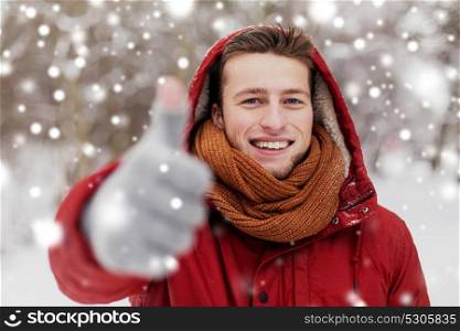 people, christmas, winter and season concept - happy smiling man in hood and scarf outdoors showing thumbs up. happy man in winter jacket showing thumbs up