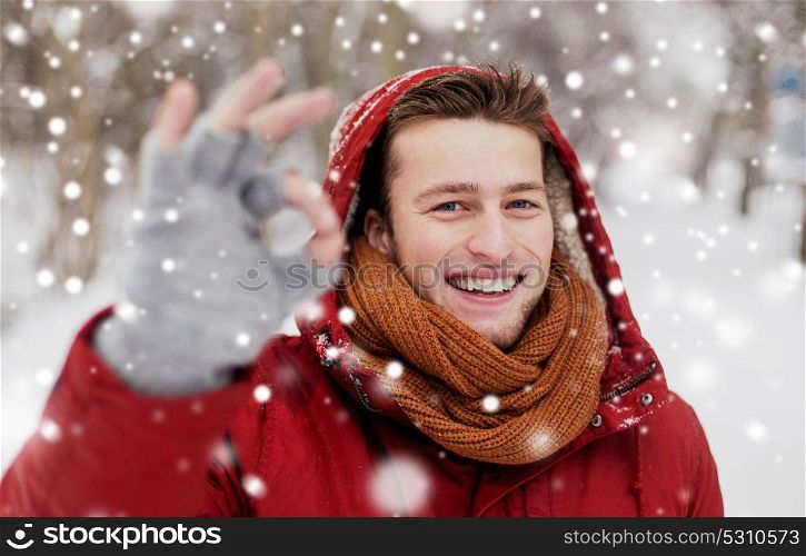 people, christmas, winter and season concept - happy smiling man in hood and scarf outdoors showing ok hand sign. happy man in winter jacket showing ok hand sign