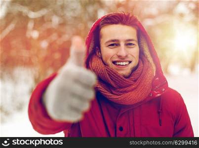 people, christmas, winter and season concept - happy smiling man in hood and scarf outdoors showing thumbs up. happy man in winter jacket showing thumbs up
