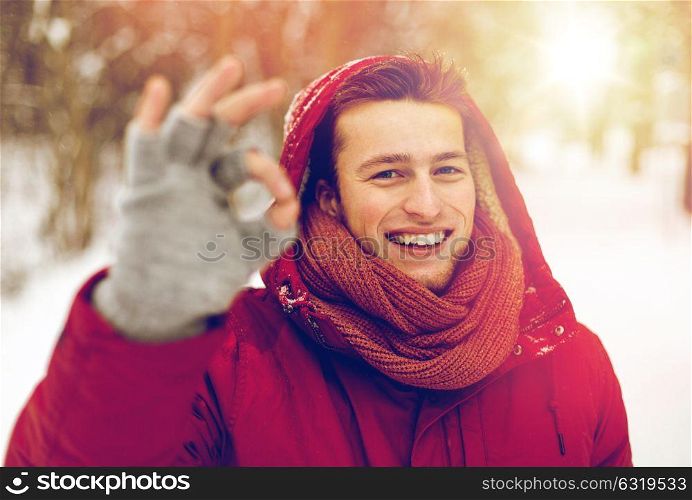 people, christmas, winter and season concept - happy smiling man in hood and scarf outdoors showing ok hand sign. happy man in winter jacket showing ok hand sign