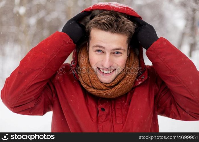 people, christmas, winter and season concept - happy smiling man in jacket and scarf wearing hood outdoors