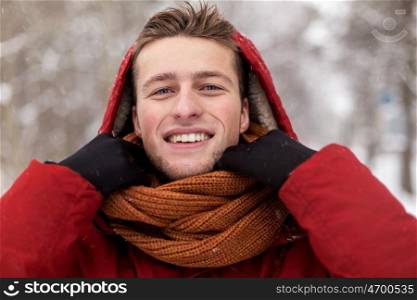 people, christmas, winter and season concept - happy smiling man in jacket with hood adjusting scarf outdoors