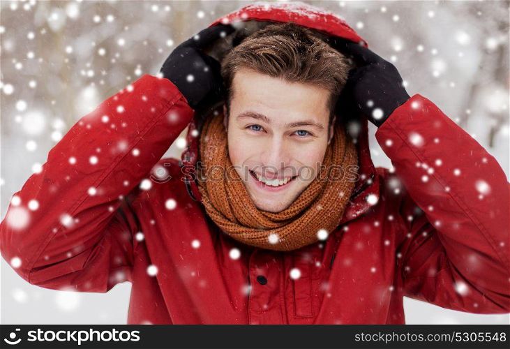 people, christmas, winter and season concept - happy smiling man in jacket and scarf wearing hood outdoors. happy man in winter jacket with hood outdoors