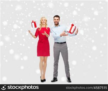 people, christmas, winter, couple and holidays concept - happy young man and woman playing with gift boxes over snow background