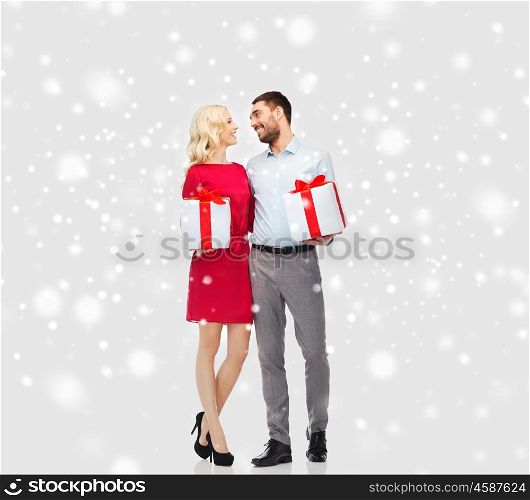 people, christmas, winter, couple and holidays concept - happy young man and woman with gift boxes over snow background