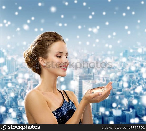 people, christmas, winter holidays and glamour concept - smiling woman in evening dress with diamond over snowy city background