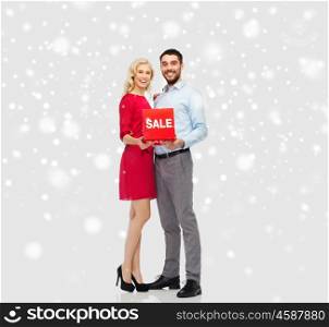 people, christmas, winter, shopping and holidays concept - happy couple with red sale sign over snow background