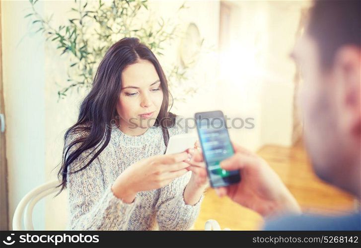 people, communication and dating concept - couple with smartphones at cafe or restaurant. couple with smartphones at cafe