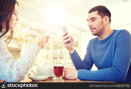 people, communication and dating concept - couple with smartphones drinking tea at cafe or restaurant. couple with smartphones drinking tea at cafe