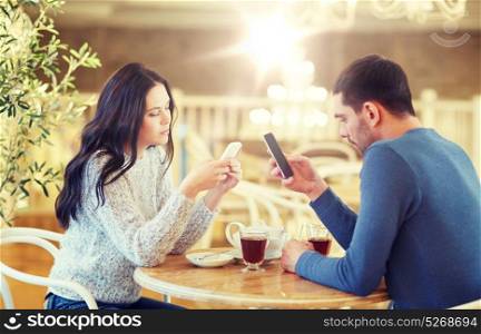 people, communication and dating concept - couple with smartphones drinking tea at cafe or restaurant. couple with smartphones drinking tea at cafe