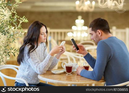 people, communication and dating concept - couple with smartphones drinking tea at cafe or restaurant