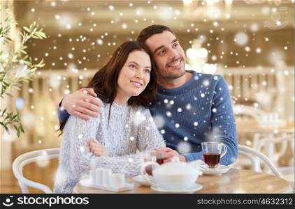 people, communication and dating concept - happy couple drinking tea and hugging at cafe or restaurant
