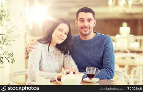 people, communication and dating concept - happy couple drinking tea and hugging at cafe or restaurant. happy couple drinking tea at restaurant