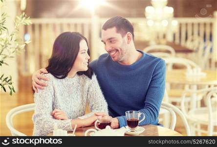 people, communication and dating concept - happy couple drinking tea and hugging at cafe or restaurant. happy couple drinking tea at restaurant