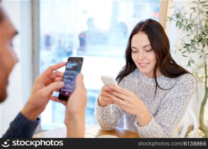 people, communication and dating concept - happy couple with smartphones at cafe or restaurant