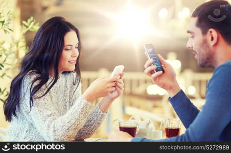 people, communication and dating concept - happy couple with smartphones drinking tea at cafe or restaurant. happy couple with smartphones drinking tea at cafe