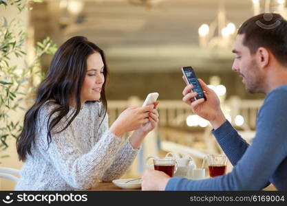 people, communication and dating concept - happy couple with smartphones drinking tea at cafe or restaurant