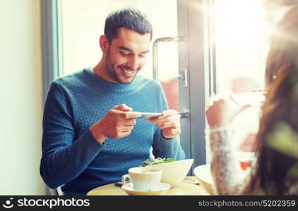 people, communication and dating concept - happy couple with smartphones picturing food at cafe or restaurant. happy couple picturing food by smartphone at cafe