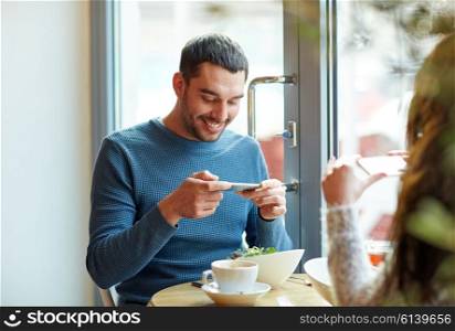 people, communication and dating concept - happy couple with smartphones picturing food at cafe or restaurant