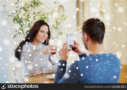 people, communication and dating concept - man with smartphone taking picture of woman drinking tea at cafe or restaurant