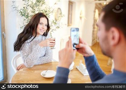 people, communication and dating concept - man with smartphone taking picture of woman drinking tea at cafe or restaurant