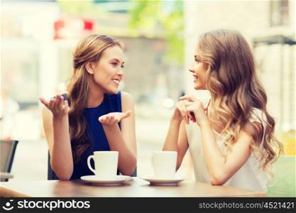 people, communication and friendship concept - smiling young women drinking coffee or tea and talking at outdoor cafe