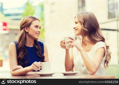 people, communication and friendship concept - smiling young women drinking coffee or tea and talking at outdoor cafe
