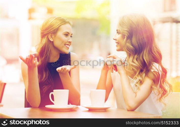 people, communication and friendship concept - smiling young women drinking coffee or tea and talking at outdoor cafe. young women drinking coffee and talking at cafe