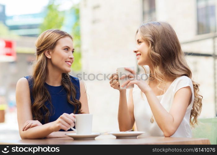 people, communication and friendship concept - smiling young women drinking coffee or tea and talking at outdoor cafe