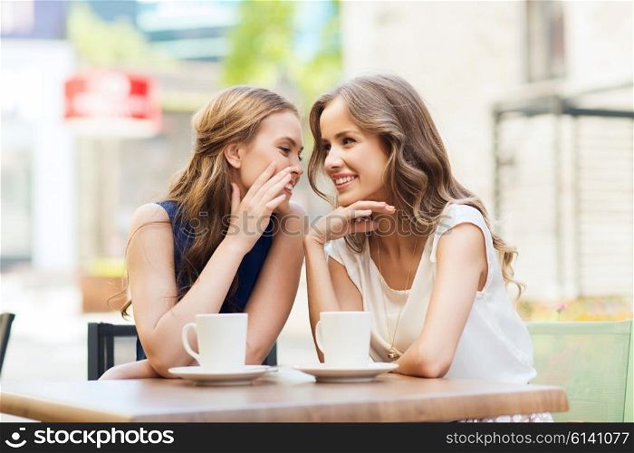 people, communication and friendship concept - smiling young women drinking coffee or tea and gossiping at outdoor cafe