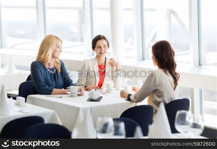 people, communication and lifestyle concept - happy women drinking coffee and talking at restaurant