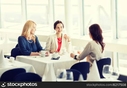 people, communication and lifestyle concept - happy women drinking coffee and talking at restaurant