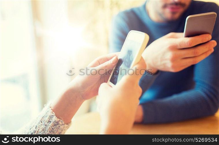 people, communication and technology concept - close up of couple with smartphones drinking tea at cafe or restaurant. close up of couple with smartphones at cafe