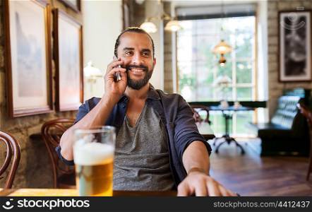 people, communication and technology concept - happy man calling on smartphone and drinking beer at bar or pub