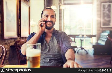 people, communication and technology concept - happy man calling on smartphone and drinking beer at bar or pub. man with smartphone and beer calling at bar or pub. man with smartphone and beer calling at bar or pub