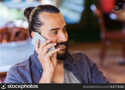 people, communication and technology concept - happy man calling on smartphone at bar or pub