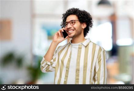 people, communication and technology concept - happy smiling man in glasses calling on smartphone over office background. happy smiling man in glasses calling on smartphone
