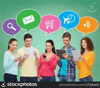 people, communication, school and technology concept - smiling friends with smartphones and tablet pc computers over green board background with doodles