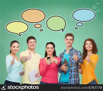 people, communication, school and technology concept - smiling friends with smartphones and tablet pc computers showing thumbs up over green board background with text bubbles