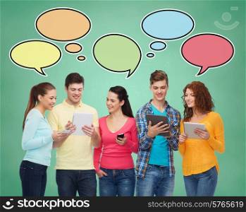 people, communication, school and technology concept - smiling friends with smartphones and tablet pc computers over green board background with text bubbles