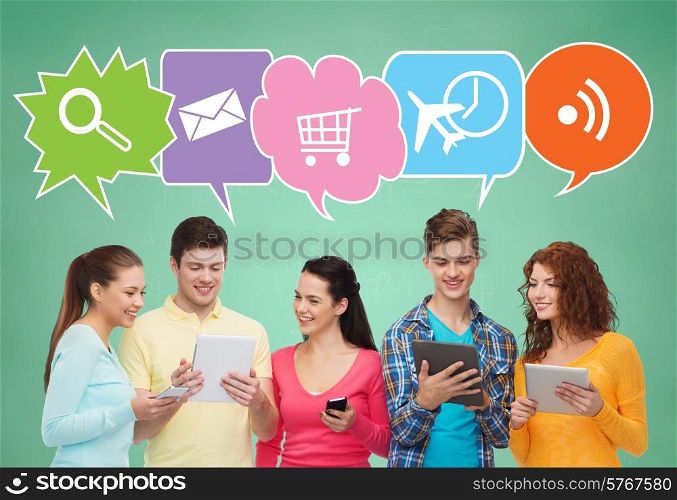 people, communication, school and technology concept - smiling friends with smartphones and tablet pc computers over green board background with text bubbles