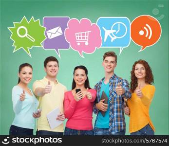people, communication, school, gesture and technology concept - smiling friends with smartphones and tablet pc computers showing thumbs up over green board background with doodles