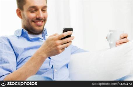 people, communication, technology and internet concept - close up of smiling man with smartphone texting or reading message and drinking tea at home