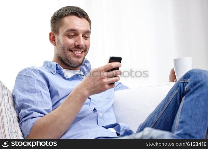 people, communication, technology and internet concept - smiling man with smartphone texting or reading message and drinking tea at home