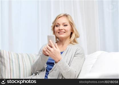 people, communication, technology and internet concept - smiling woman with smartphone texting at home