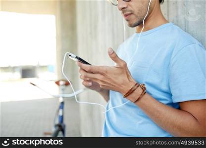 people, communication, technology and lifestyle - close up of hipster man with smartphone, earphones and fixed gear bike listening to music on city street. man with earphones and smartphone listening music