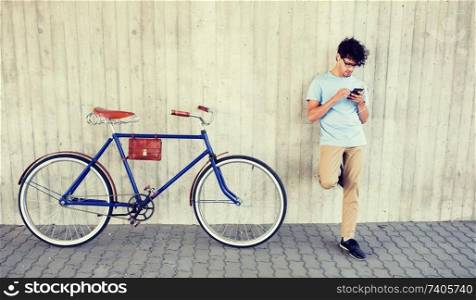people, communication, technology, leisure and lifestyle - hipster man with smartphone and earphones on fixed gear bike listening to music on city street. man with smartphone and earphones on bicycle