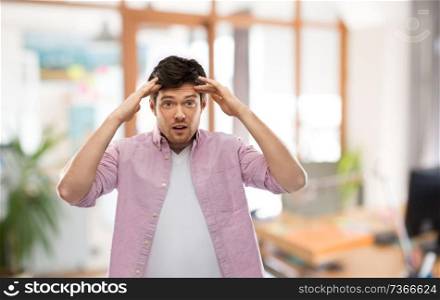 people, concentration and mind concept - man touching his head over office room background. man touching his head over office room